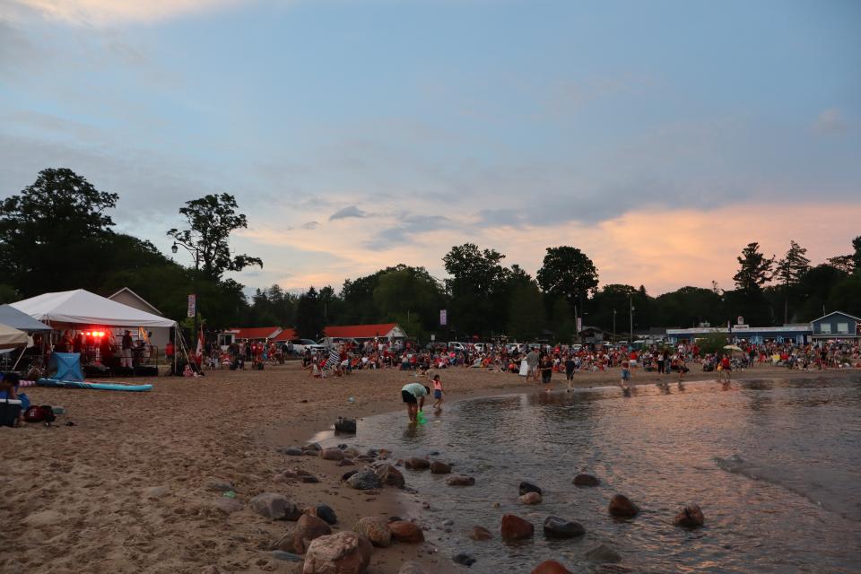 View of the entertainment tent and a large crowd on Balm Beach near sunset with the water and sand in the foreground.