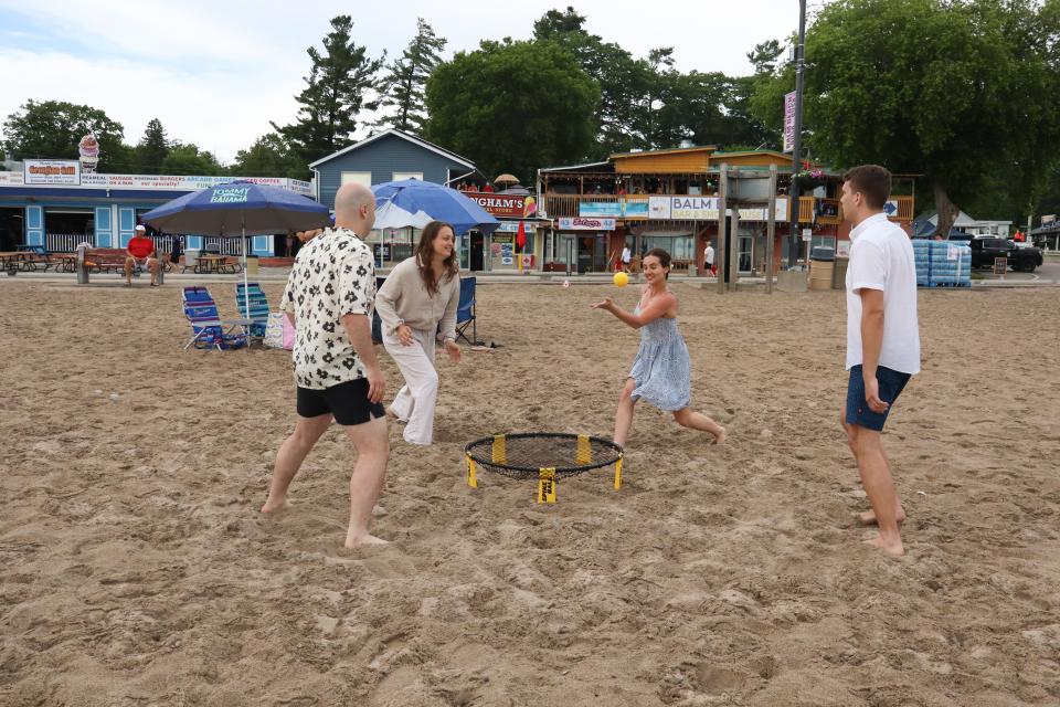 Group of four adults playing spike ball with one of the women in a blue dress about to hit the ball.