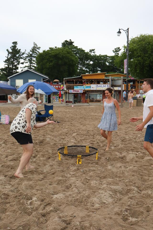 Group of four adults playing spike ball with one of the men about to hit the yellow ball.