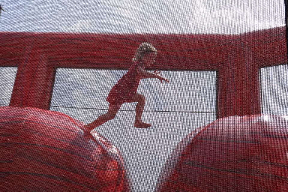Child mid jump from one red ball to another inside a large bouncy castle with mesh caging for protection.