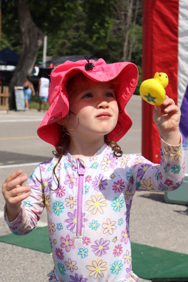 Child holding up a yellow rubber duck wearing a bright pink hat and multi-coloured flower outfit.
