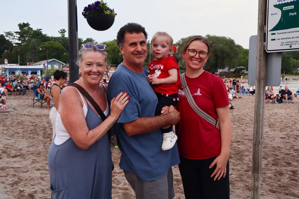 Group of three adults with the man in the middle holding a young child with red flashing lights