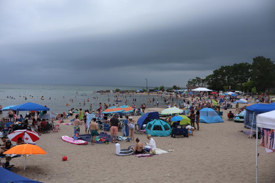 View of a busy Balm Beach filled with people and colourful umbrellas prior to rain moving into the area marked by dark skies