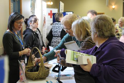 A group of older adult ladies picking up information at a booth at the Senior Symposium event