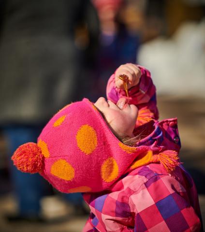 Girl licking maple taffy while hovering it over her face