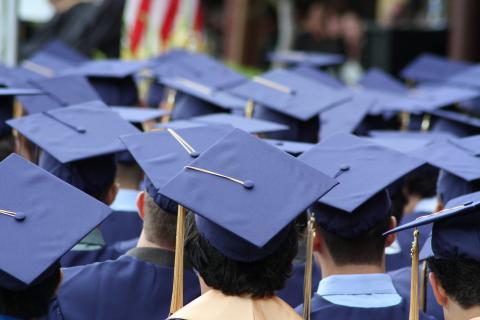 Students in graduation gowns and caps sit during their ceremony