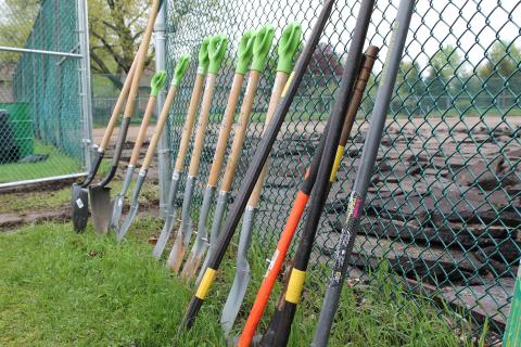 Shovels leaning against a chain link fence with broken chunks of asphalt behind 