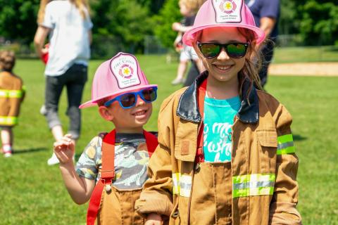 Two children wearing sunglasses and firefighter costumes smile and post for the camera