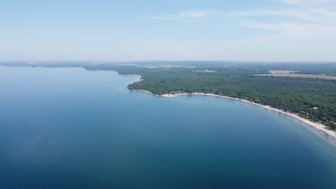 Drone photo overlooking beach coastline with blue water and green foliage off the beach