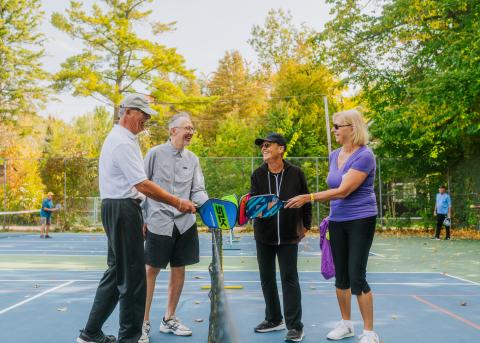 image of two people on each side of the pickleball net, putting their paddles together on a nice sunny day