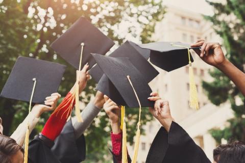 several students' arms lifting graduation caps into the air