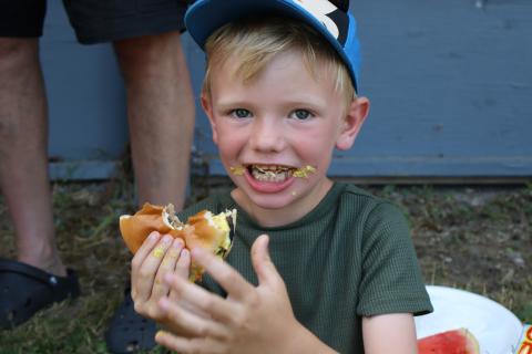 young boy after taking a large bite of their burger with condiments on their face