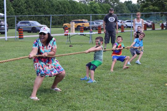 mother with several kids in bright clothing participating in a game of tug of war with other residents watching in the background