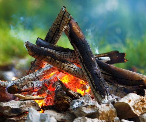 campfire with rocks around it and the logs half burnt stacked in a pyramid shape