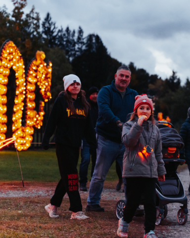 young family with a stroller walking down the pathway in the evening with lit up pumpkins in the background