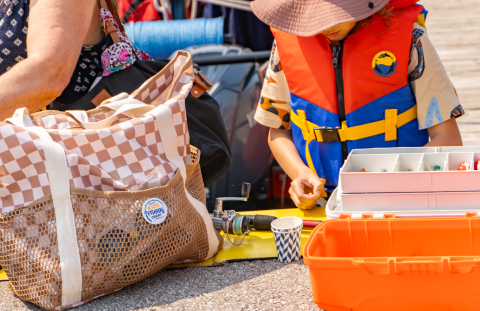 A child wearing a life jacket and looking inside a fishing tackle box