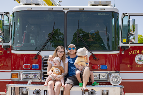 Two adults and two children sitting on the front of a Town of Midland Fire Truck