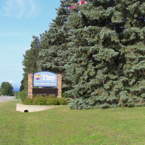Township of Tiny office sign with large green evergreen trees