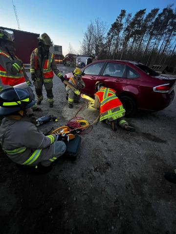 Tiny firefighters training on an older model sedan performing an auto extrication rescue simulation