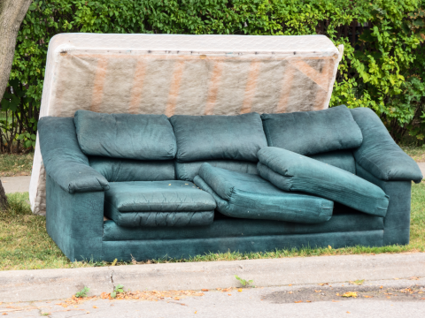 Green 3-seater couch with cushions not sitting in place and box spring leaning on the back of the couch on the side of the road