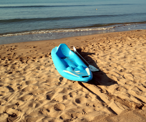 bright blue kayak and paddle sitting on the sand of an empty beach with calm waves coming onto shore