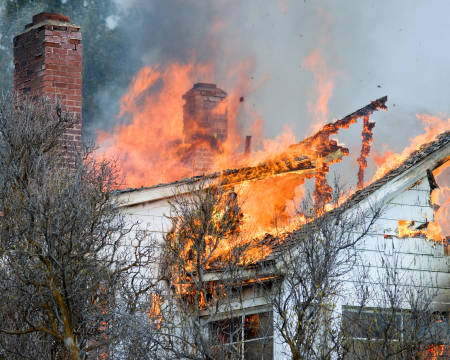 A house with white siding and two brick chimneys with the roof on fire.