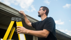 man on a step ladder checking the roof of their house