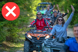 Group of riders and various ATVs and SxS not wearing helmets waving to the camera on a wooded pathway