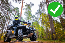 ATV rider on a black and yellow ATV wearing a bright neon helmet on a forest trail